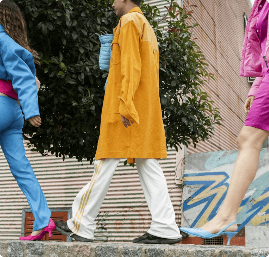 Three people walking across the screen. The one in the middle is wearing a long yellow trench coat
